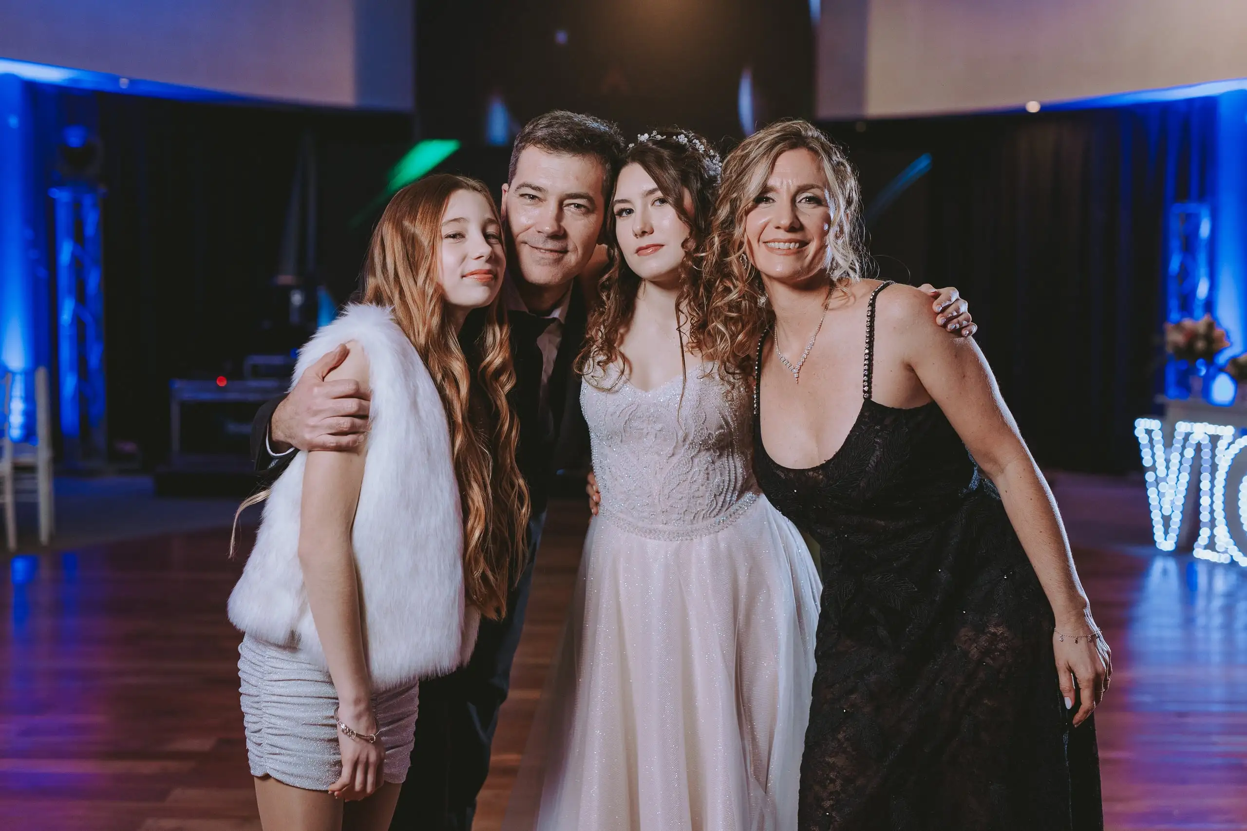 La quinceañera abrazada por su familia en la pista, con luces azules de fondo.