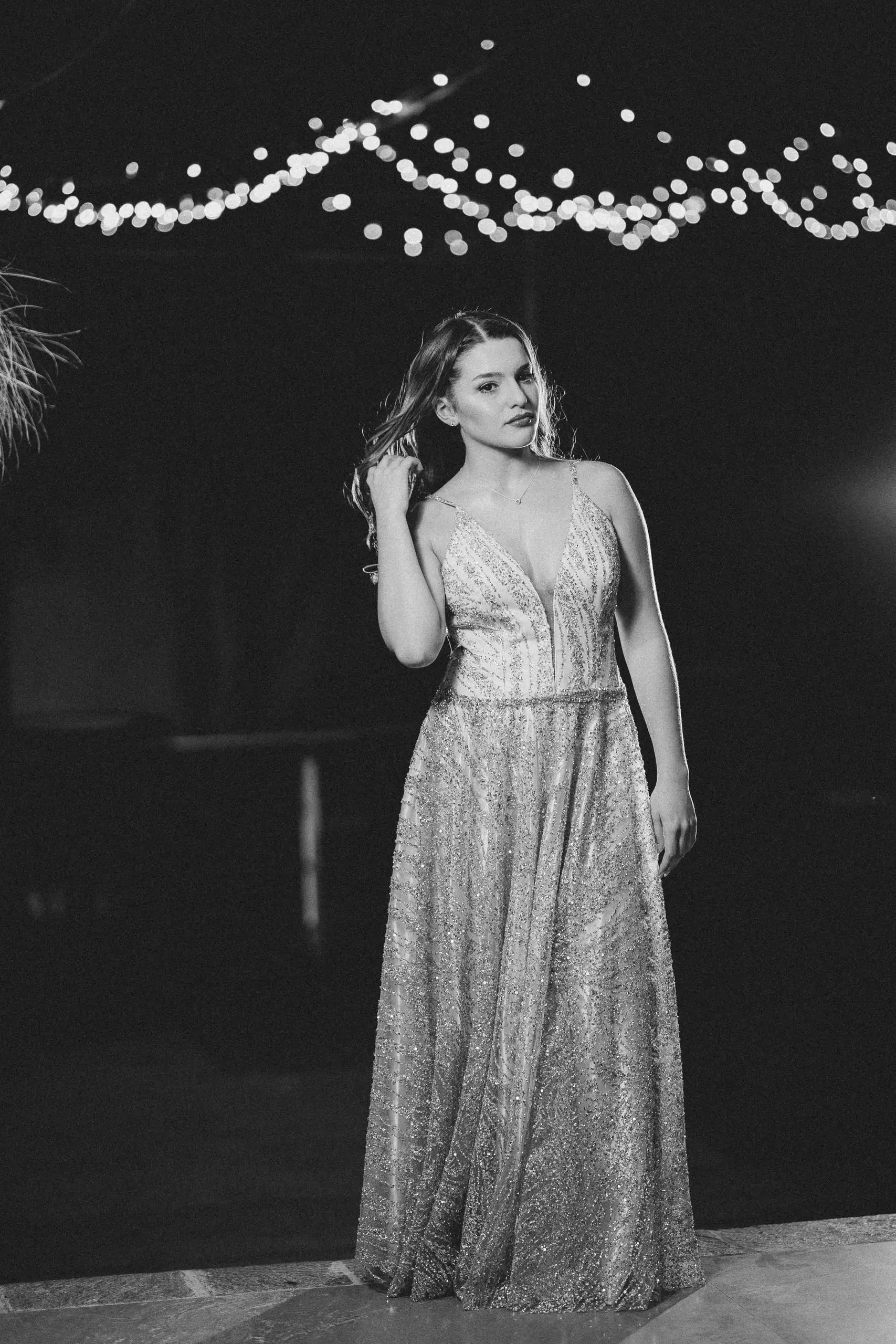 Retrato en blanco y negro de la quinceañera con vestido brillante, bajo una guirnalda de luces.