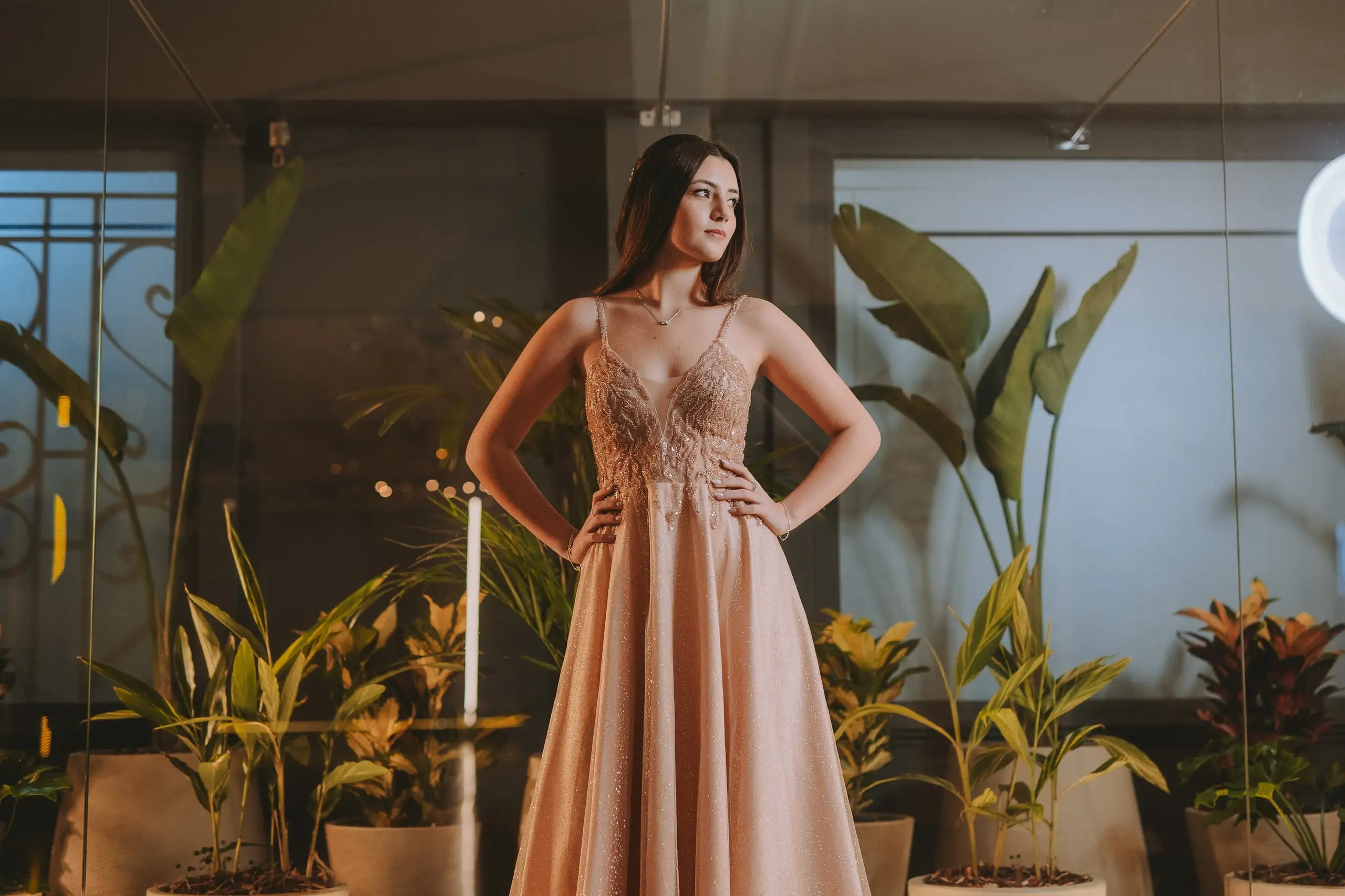 La quinceañera, con vestido rosado de tul, posa entre plantas tropicales.