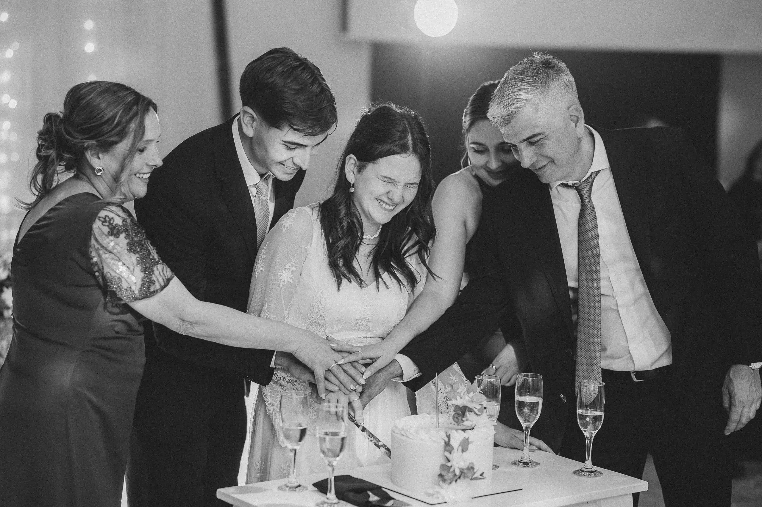 En blanco y negro, la quinceañera y su familia cortan juntos la torta, entre copas de champagne.
