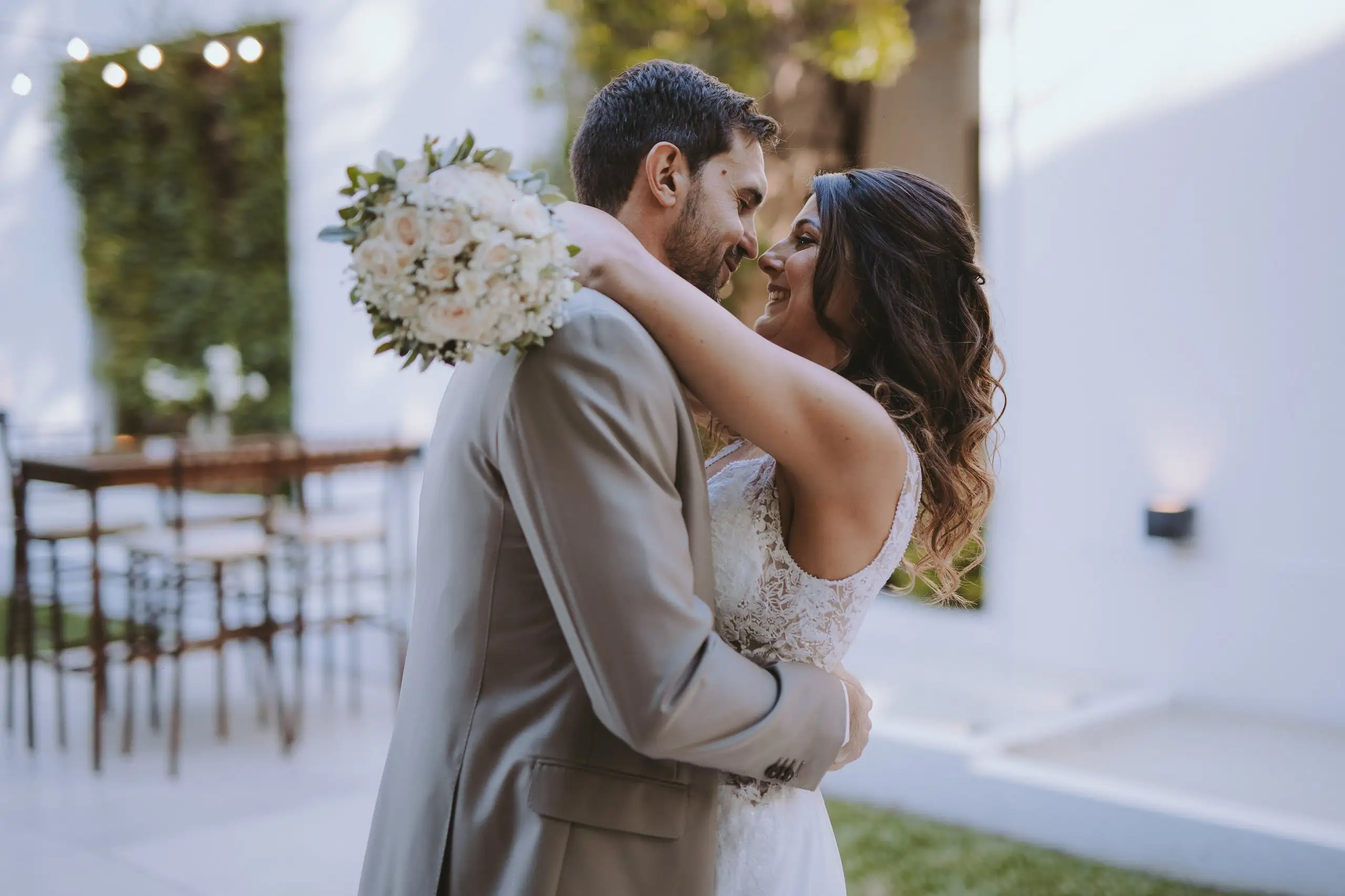 Los novios abrazados se miran de cerca; ella apoya el ramo de rosas blancas sobre el hombro de él.