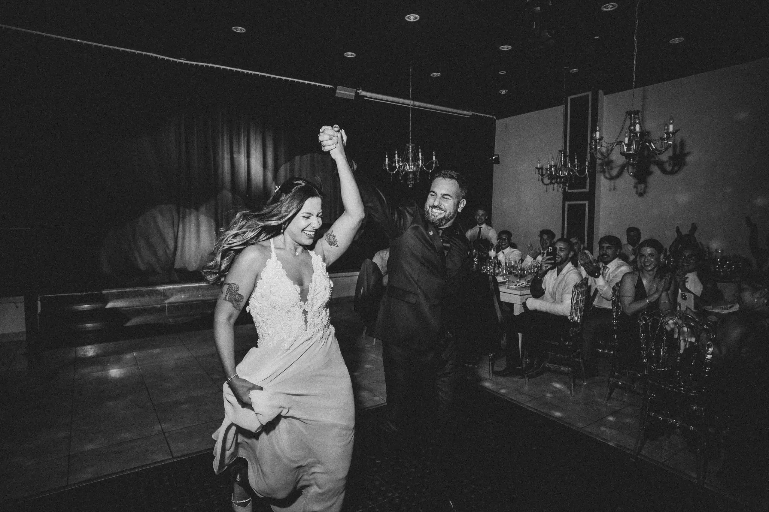 En blanco y negro, los novios entran bailando al salón con los brazos en alto frente a los invitados.