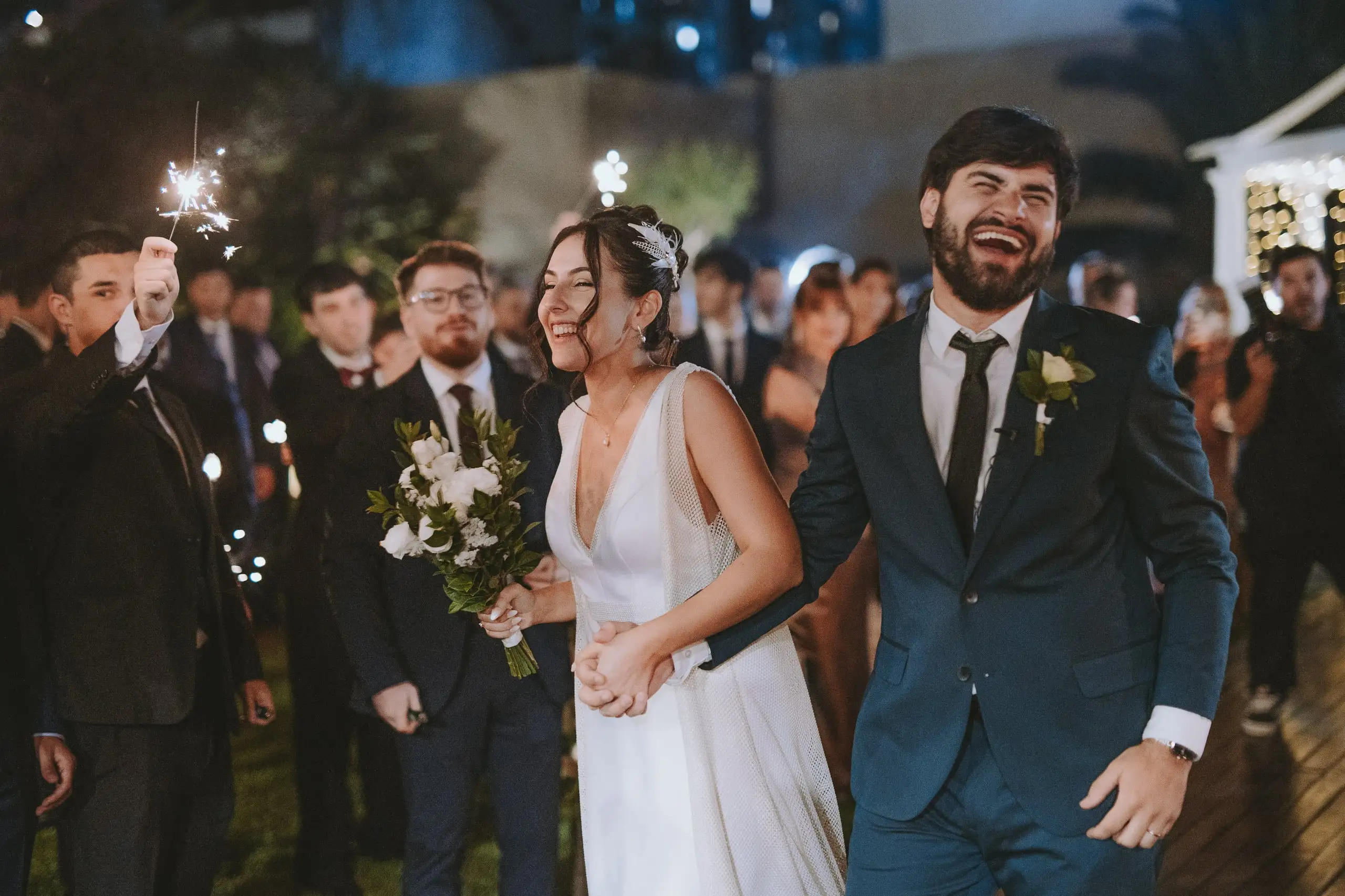 Los novios ríen a carcajadas al salir entre invitados que sostienen bengalas encendidas.
